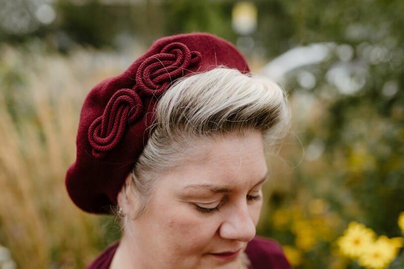 Milliner Sophie Cooke wearing a wine red beret with a wine cord knot from the new AW23 Beret collection