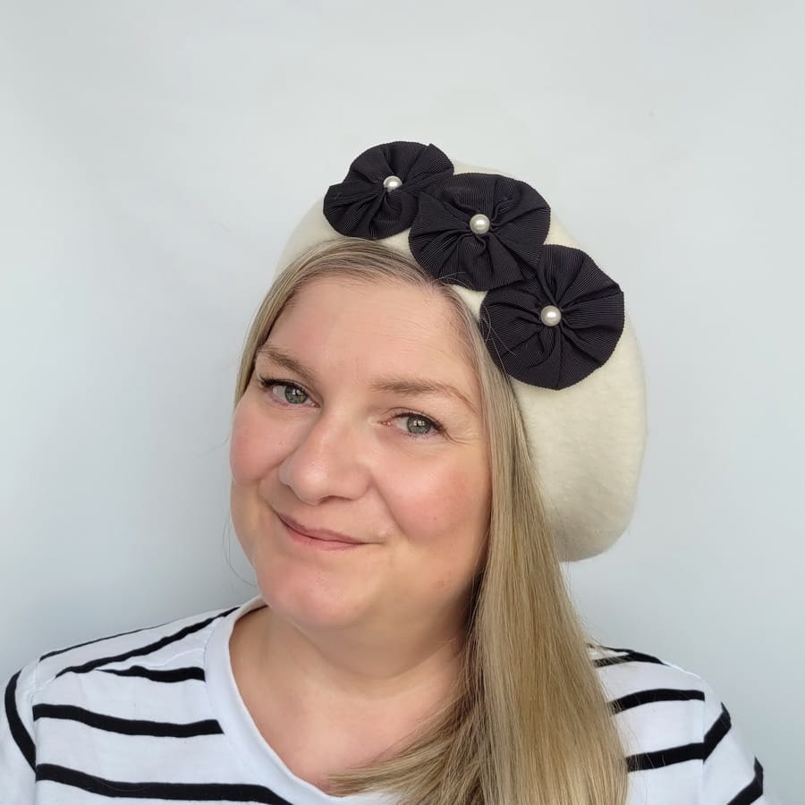 Ivory Beret with Ribbon Rosettes and Pearls worn by a white woman in her 40s with long blonde hair